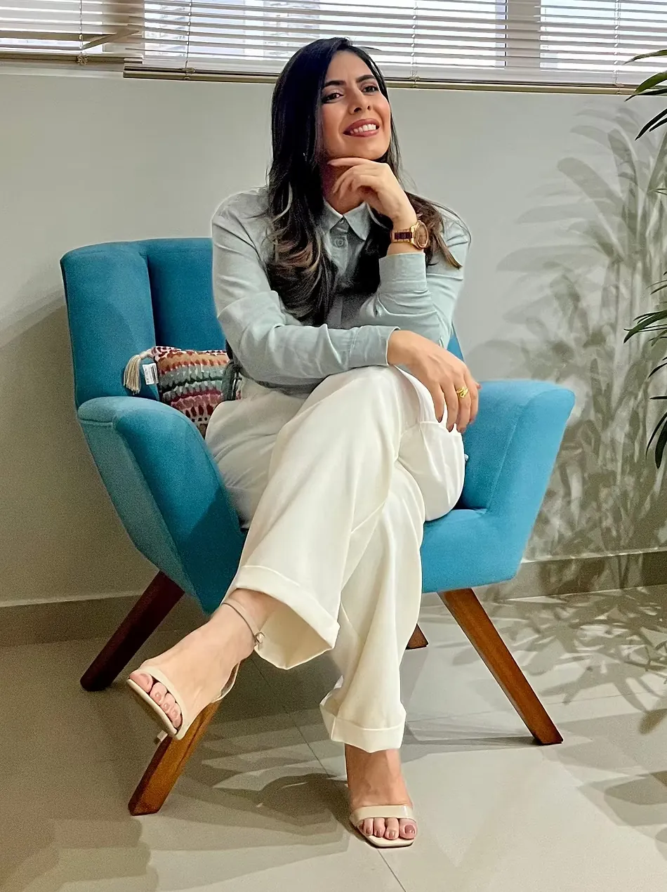 Thaiza Leandro sorrindo, sentada em uma poltrona azul no consultório.